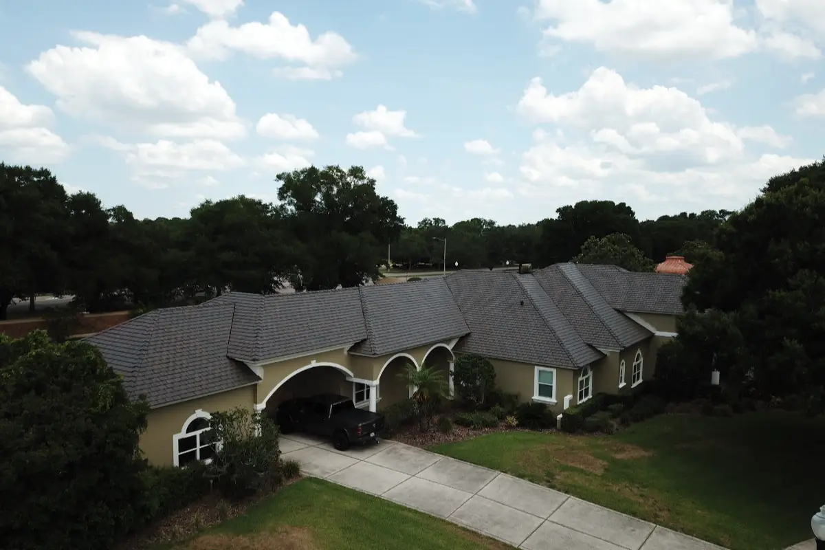 Drone photo of large single-story home with dark shingle roof and arched entryway