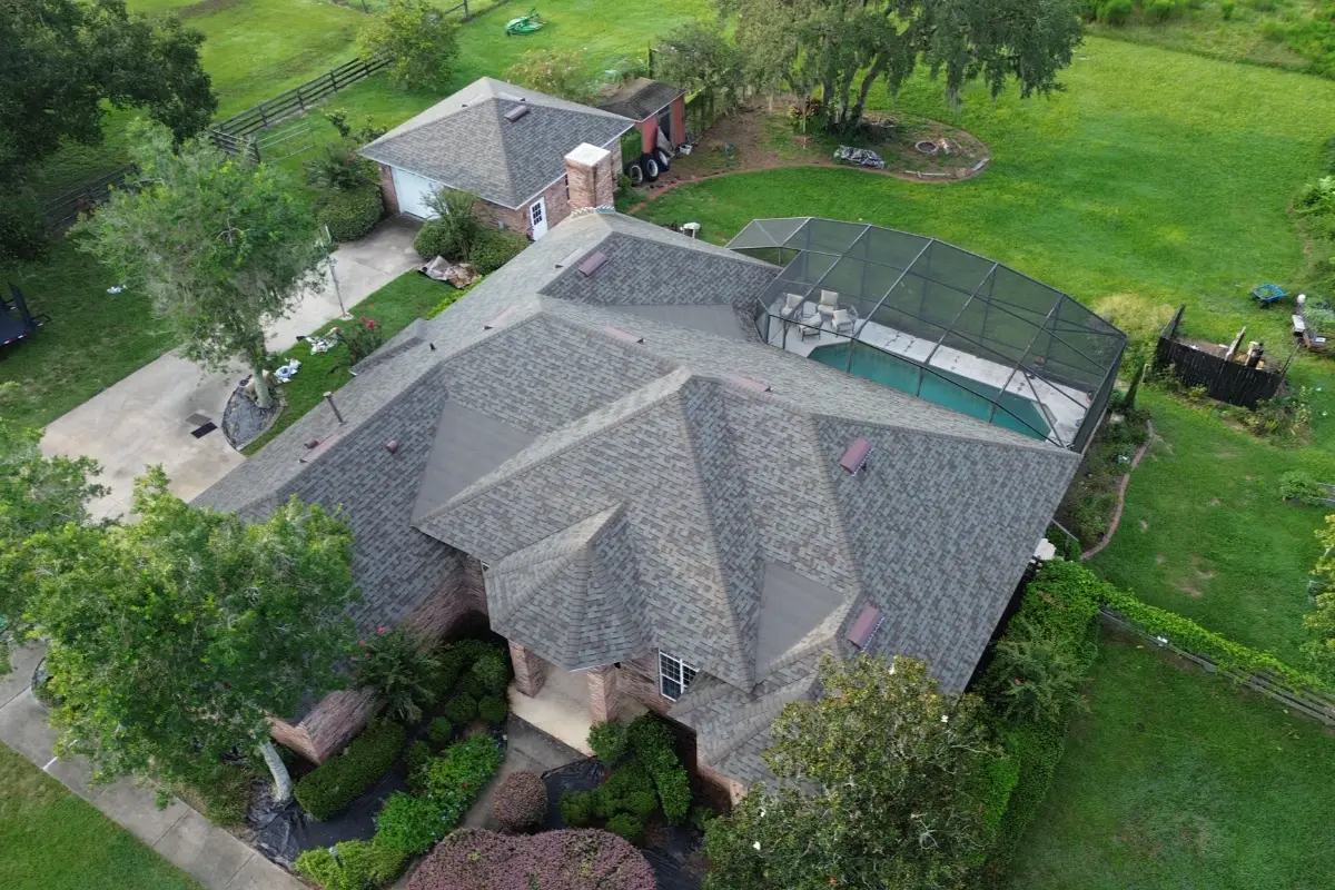 Aerial view of residential asphalt shingle roof with multiple rooflines and landscaped yard