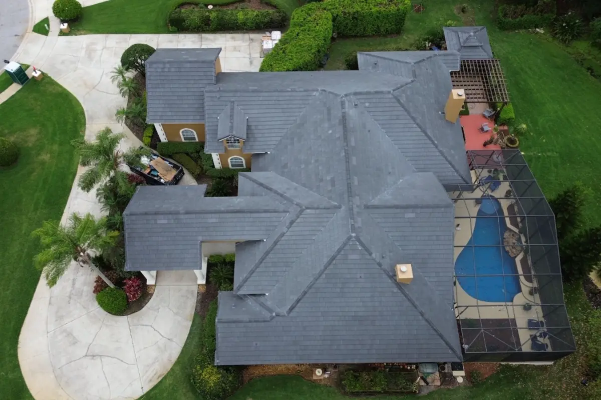 Aerial view of residential home with newly installed gray shingle roof, driveway, landscaped yard, and surrounding greenery