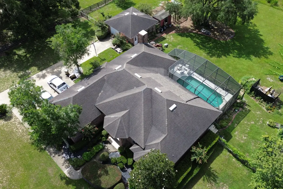 Aerial view of large residential property featuring a completed gray shingle roof, screened pool enclosure, detached garage, and landscaped grounds